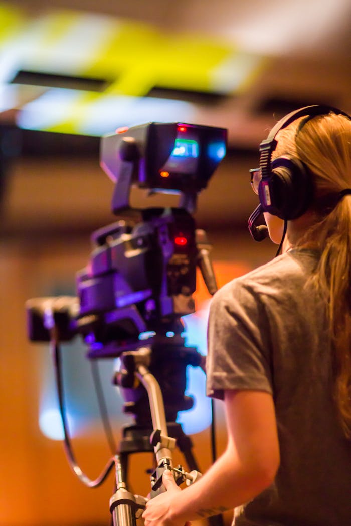 A woman operates a professional camera indoors, focusing on media production.